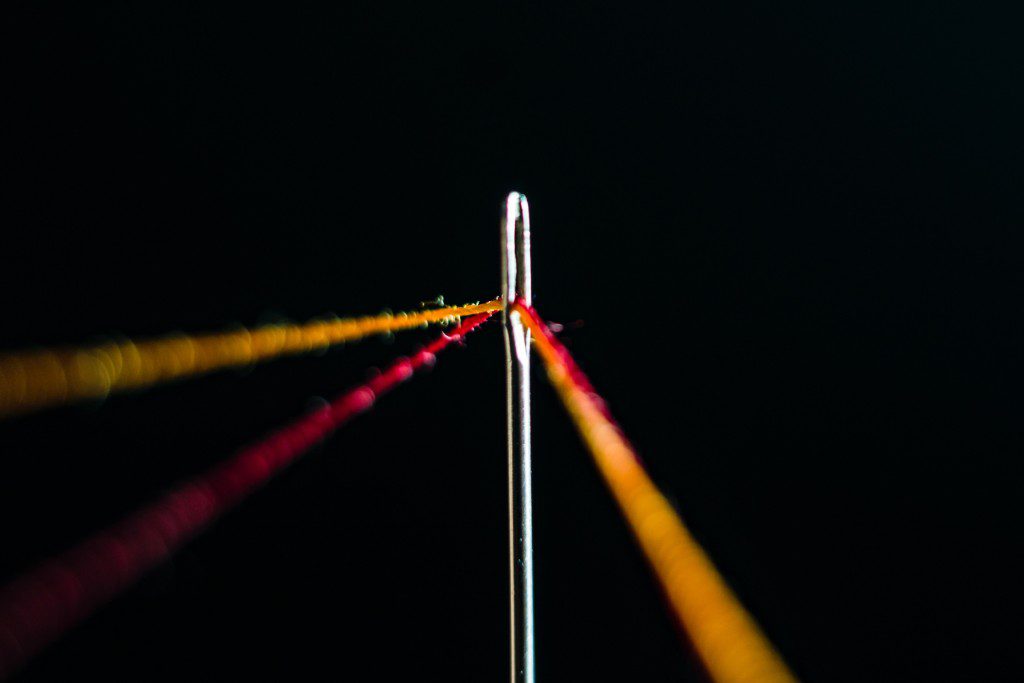 Close-up of a needle with colorful threads against a black background